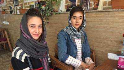 Kvinnorna Shaqaiq och Arzoo ler mot kameran på ett kafé i Kabul.