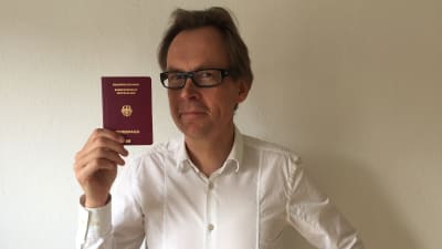 Kaj Arnö i vit skjorta och med tyskt pass i handen som han håller upp.