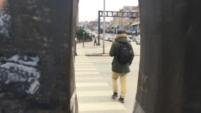 En ung man går över gatan, fotad genom en springa så att han ser inklämd ut