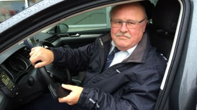 En man sitter i en taxibil. Han heter Stig-Erik Holmström och är taxichaufför.