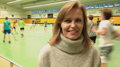 Lena Törnqvist står inne i Aurorahallen, med innebandyspelare i bakgrunden