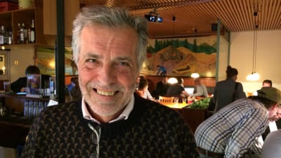 Glad man med restaurangbesökare i bakgrunden.