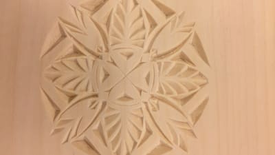 En ljus träskiva som dekorerats med ett runt ornament i träsnitt.