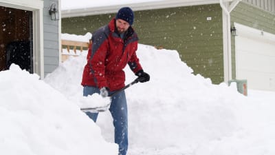 En man skyfflar snö utanför en villa.