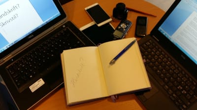 Datorer, telefoner, en padda och ett skrivhäfte ligger på ett bord.