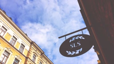 SLS metallskylt på Riddaregatan i Helsingfors fotograferad underifrån mot en blå himmel. 