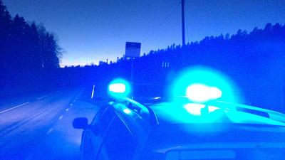 Bil med blåljus kör i mörker på landsväg.