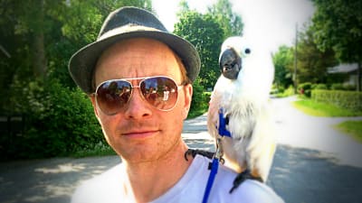 Filmregissören Dome Karukoski, en av vegas sommarpratare 2014 har en vit papegoja på axeln. I solglasögonen speglas fotografen och en vän. Det är sommar