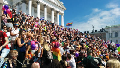 Trapporna till Helsingfros domkyrka på Senatstorget är fullsatta av pridedeltagare med regnbågsflaggor och ballonger.