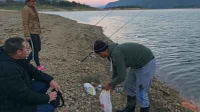 Tre personer fiskar i en by i Bosnien. 
