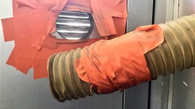 Ett ventilationsrör som har tejpats fast i en dörr med orangefärgad tejp. Men röret har lossnat.