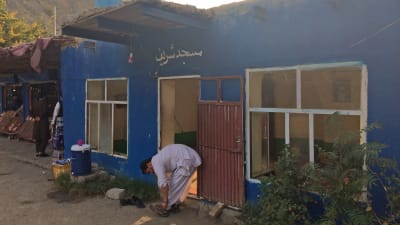 En muslimsk man knyter skorna framför ett blått hus i Afghanistan.