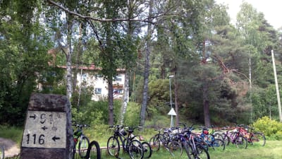 Cyklar utanför en byskola, grönt gräs, i förgrunden en gammal milstolpe.
