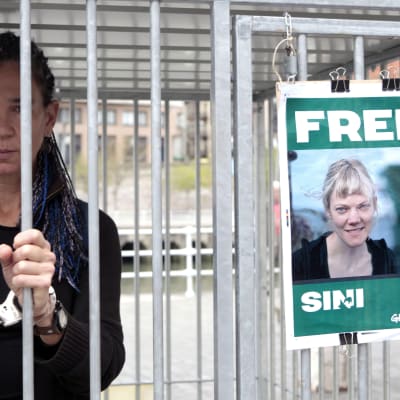 Henkilö kaltereiden takana, kaltereissa juliste.