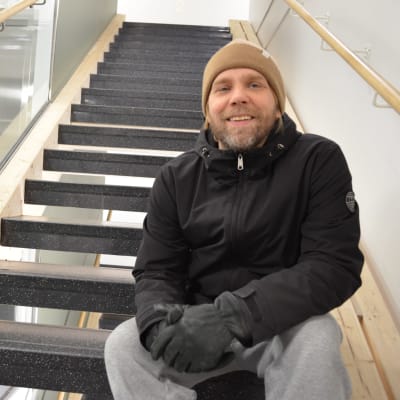 Mies istuu kerrostalon rappukäytävässä portailla.