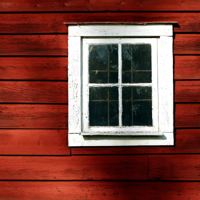 en rödmålad stockvägg med ett vitmålat fyrkantigt fönster med fyra mindre rutor