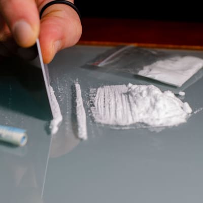 Kokaiiniviivoja pöydällä. Kuvassa näkyy käsi, joka pilkkoo ainetta.