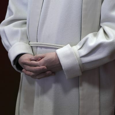 En präst som står med knäppta händer