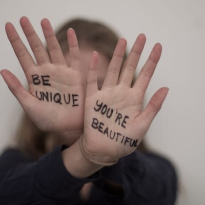 Två händer som hålls upp med texten "be unique" och "you're beautiful" skrivna på handflatorna.