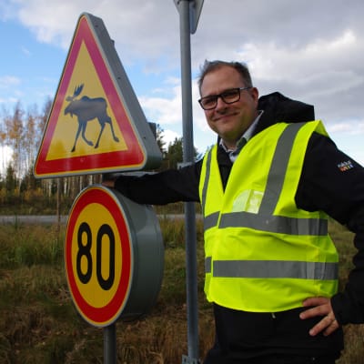 En man i reflexväst står vid en trafikskylt.