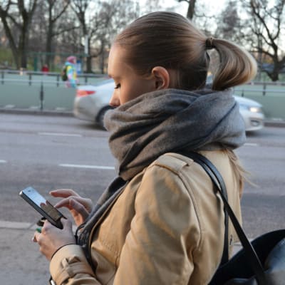 Kvinna går på stan och kollar på sin smarttelefon.