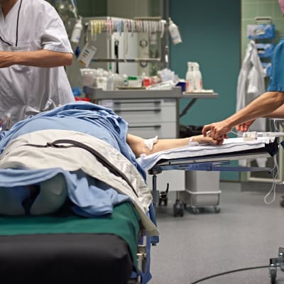 En patient ligger på en säng i en operationssal. Runtom står vårdpersonal.