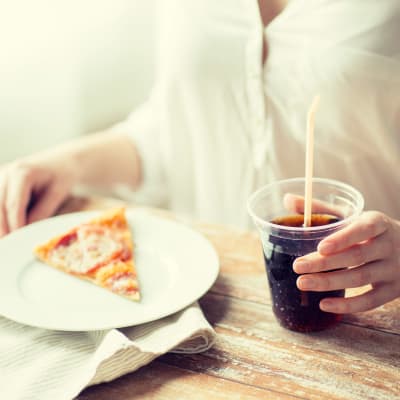 En kvinna äter pizza och dricker coca cola.