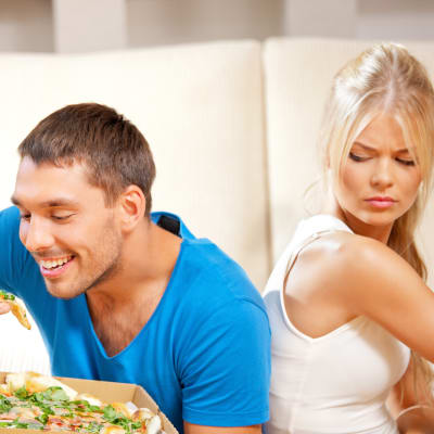 kvinna med äpple i handen tittar irriterat på glad man som äter  pizza