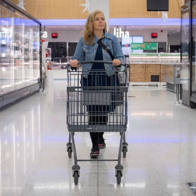 Nainen kävelee ostoskärryjen kanssa kylmäkaappien välissä.