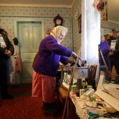 Äldre kvinna röstar i parlamentsvalet i Ukraina, i närvaro av en medlem av valkommissionen.