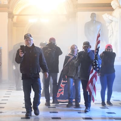 Demonstranter kommer gåendes mot kameran i Kapitolium. En håller upp sin telefon och filmar, andra bär flaggor.