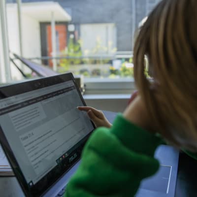 Skolelev i grön huvtröja sitter vid en dator.