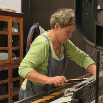 En kvinna, Ülle Nurmi, står koncentrerat vid en gammal vävmaskin och jobbar.