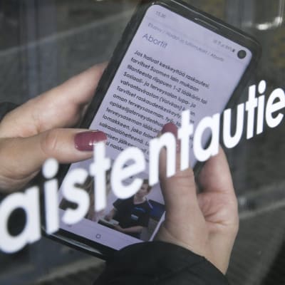 En person håller i en mobiltelefon med en finspråkig text om abort.