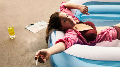 En ung kvinna i rosa skjorta ligger bakåtlutad i en gummibassäng med en cigarett i handen.