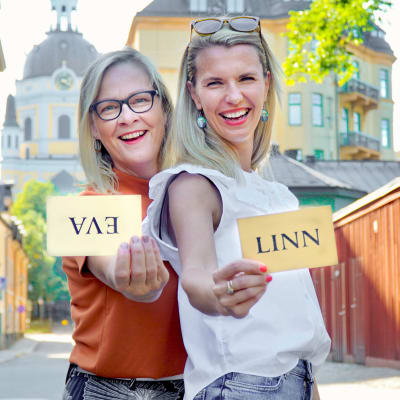 Eva Biaudet och Linn Jung på solig trähusgata i Stockholm med handskrivna namnlappar i händerna. Evas lapp är uppochned.