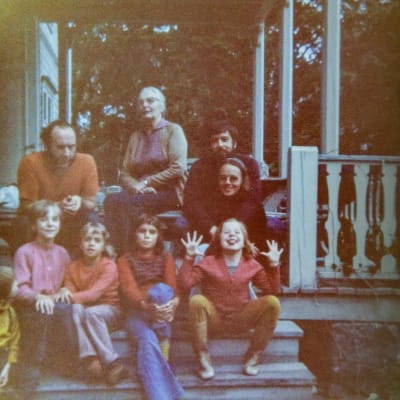 Vuxna och barn sitter på en trappa. Flickan längst till höger visar tungan och spretar med fingrarna.