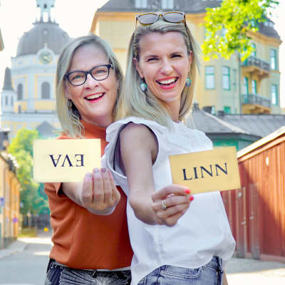 Eva Biaudet och Linn Jung på solig trähusgata i Stockholm med handskrivna namnlappar i händerna. Evas lapp är uppochned.