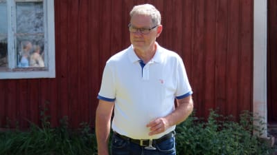 Stefan Friman står på gräsmattan utanför ett rödmålat hus en solig sommardag.