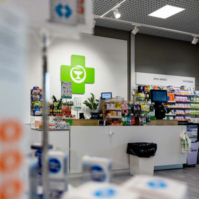 Interiör från ett apotek, kassa med en stor grön logotyp på väggen. 