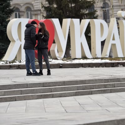 Ett ungt par kysser varandra framför en skylt med den ukrainska texten "jag älskar Ukraina".