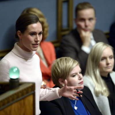 Sanna Marin pratar i ministerbåset i plenisalen, Annika Saarikko och Maria Ohisalo i bakgrunden.