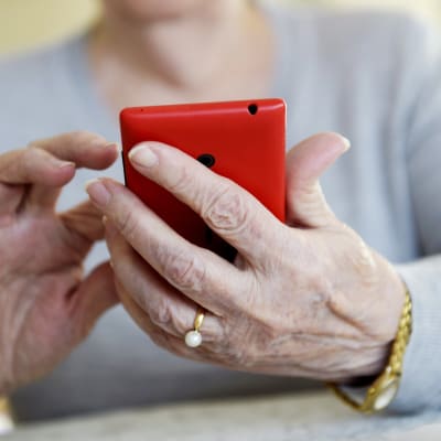 En äldre kvinna håller en röd smarttelefon i handen.