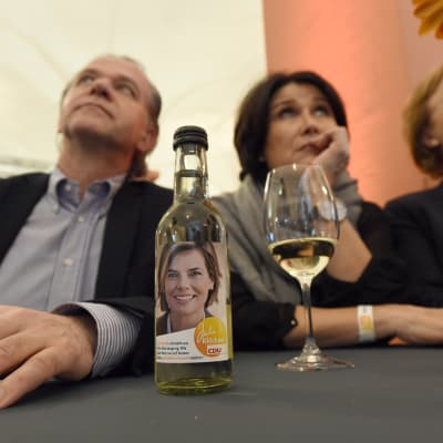 CDU-anhängare reagerar på valresultatet i Tyskland. Supportrarna sitter bakom en vinflaksa med en bild på en av CDU-kandidaterna Julia Kloeckner.