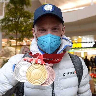 Iivo Niskanen håller upp sina tre OS-medaljer på flygplatsen i Helsingfors.
