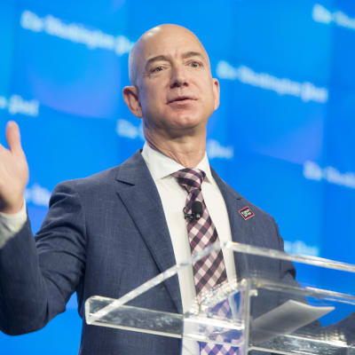 Jeff Bezos bakom genomskinlig talarstol med utsträckta händer