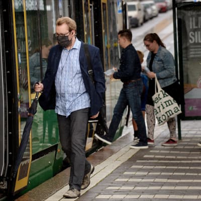 En man stiger på spårvagnen i centrala Helsingfors. Han bär ett svart munskydd.