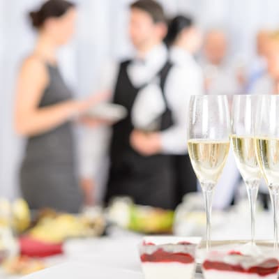 En bricka med champagne eller mousserande vin står på ett bord. I bakgrunden synd flera personer i festkläder.