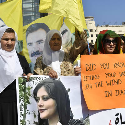 Kvinnor håller i en utprintad bild av Mahsa Amini och skyltar medan de demonstrerar.