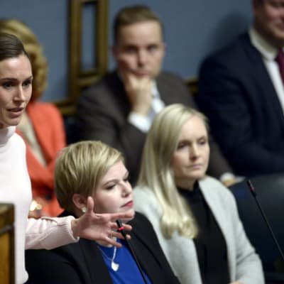 Sanna Marin pratar i ministerbåset i plenisalen, Annika Saarikko och Maria Ohisalo i bakgrunden.